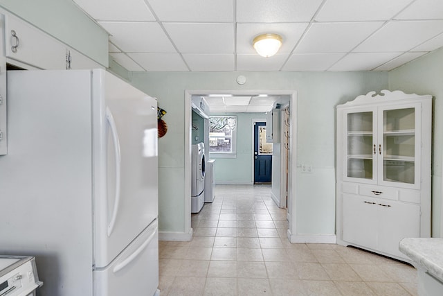 kitchen with a drop ceiling, washing machine and dryer, freestanding refrigerator, white cabinets, and baseboards