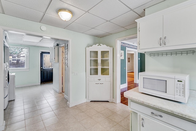 kitchen with white microwave, white cabinetry, light countertops, a paneled ceiling, and washer and dryer