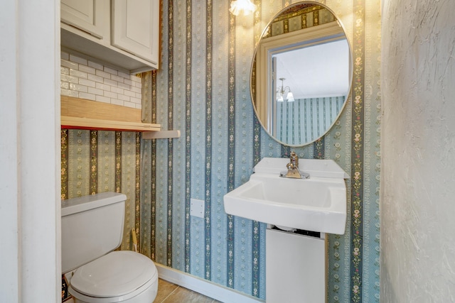 half bathroom featuring toilet, wallpapered walls, and a sink