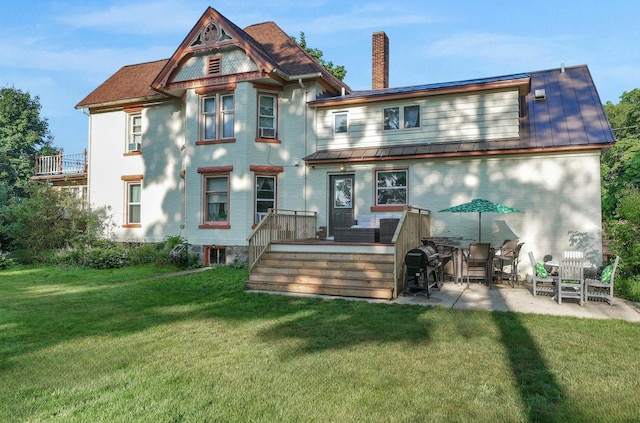 back of house featuring a patio, a lawn, a chimney, and metal roof