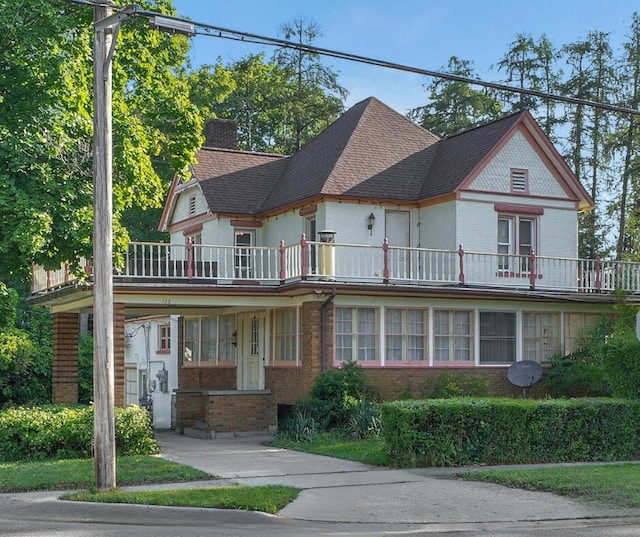 view of front of house with a shingled roof, a balcony, brick siding, and a chimney