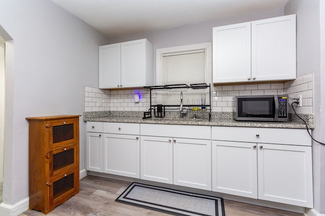 kitchen featuring light stone countertops, sink, tasteful backsplash, white cabinets, and light wood-type flooring