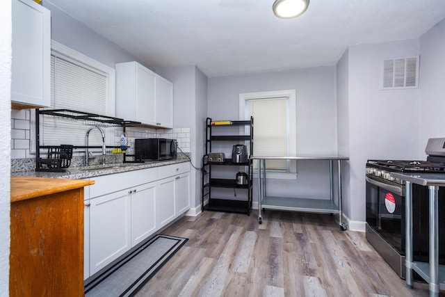 kitchen featuring backsplash, sink, light hardwood / wood-style floors, white cabinetry, and stainless steel range with gas stovetop