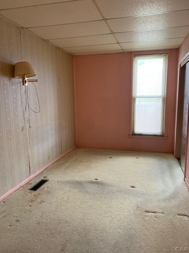 carpeted empty room featuring a paneled ceiling and wooden walls