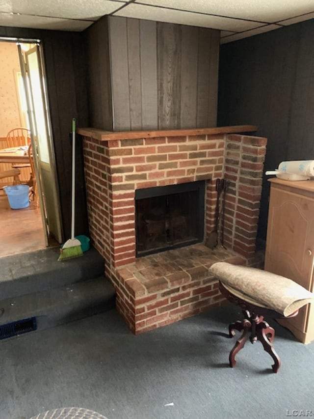 interior details featuring carpet flooring, a paneled ceiling, a brick fireplace, and wooden walls