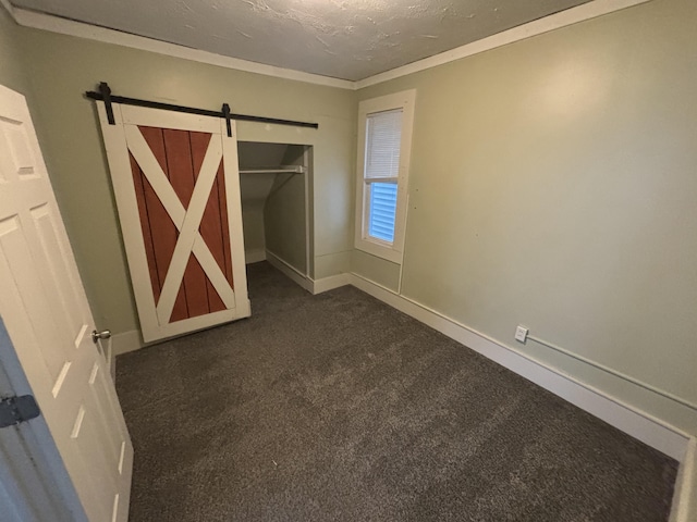 unfurnished bedroom with a barn door, a textured ceiling, a closet, dark carpet, and ornamental molding