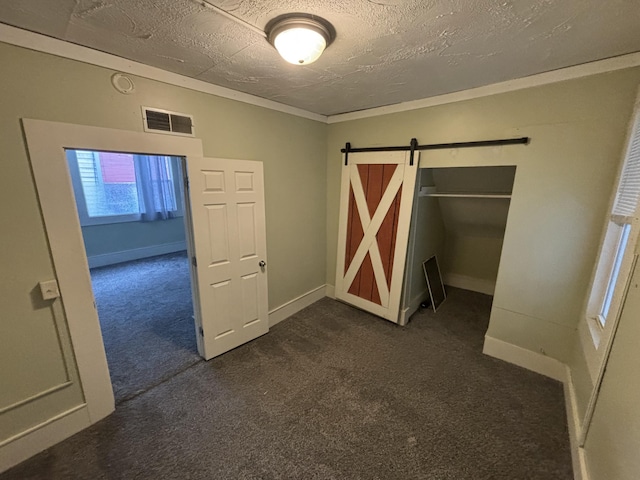 interior space with a textured ceiling, crown molding, dark colored carpet, a barn door, and a closet