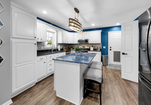 kitchen with hanging light fixtures, white cabinets, dark hardwood / wood-style flooring, a kitchen island, and appliances with stainless steel finishes