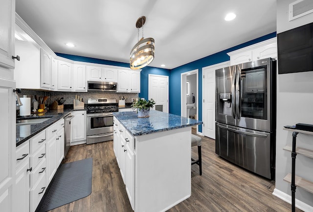 kitchen featuring tasteful backsplash, stainless steel appliances, decorative light fixtures, white cabinets, and a center island