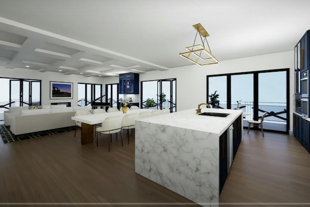 kitchen featuring coffered ceiling, sink, hanging light fixtures, light stone countertops, and an island with sink