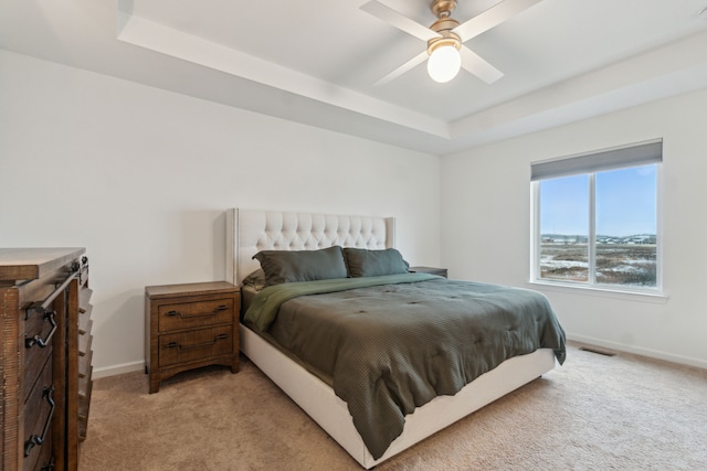 bedroom featuring ceiling fan, light carpet, and a tray ceiling