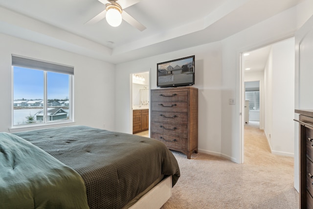 carpeted bedroom featuring ceiling fan, ensuite bath, and a tray ceiling