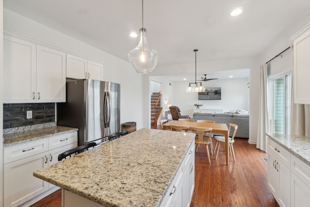 kitchen with pendant lighting, stainless steel fridge, light stone countertops, a kitchen island, and white cabinetry