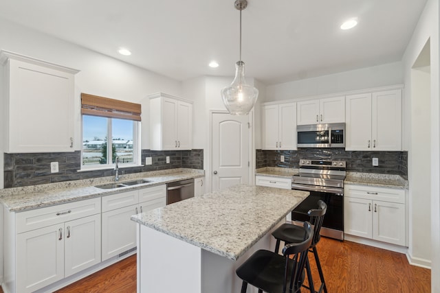 kitchen with a center island, sink, hanging light fixtures, white cabinets, and appliances with stainless steel finishes