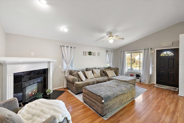 living room with ceiling fan, light wood-type flooring, a fireplace, and vaulted ceiling