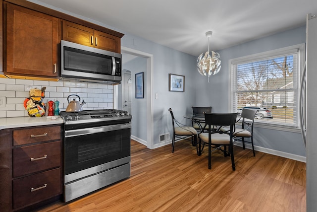 kitchen featuring decorative backsplash, appliances with stainless steel finishes, pendant lighting, a notable chandelier, and light hardwood / wood-style floors