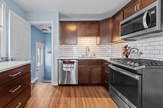 kitchen featuring decorative backsplash, dark brown cabinetry, stainless steel appliances, sink, and light hardwood / wood-style floors