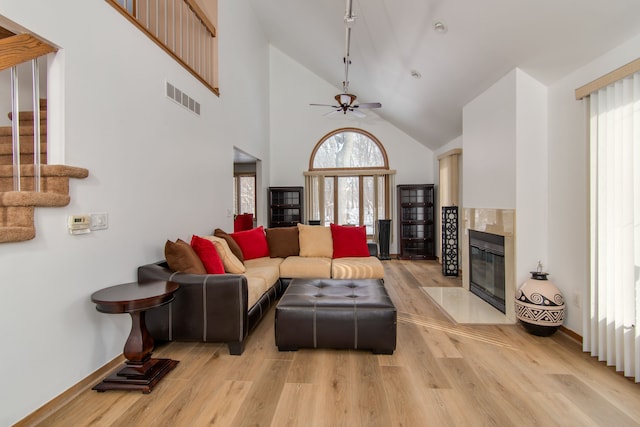 living room with a fireplace, a high ceiling, ceiling fan, and light wood-type flooring