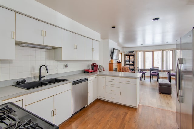 kitchen with appliances with stainless steel finishes, white cabinetry, sink, kitchen peninsula, and light hardwood / wood-style flooring