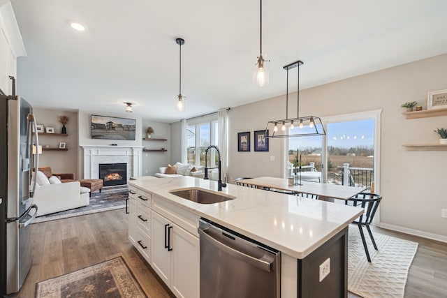 kitchen with white cabinetry, sink, stainless steel appliances, pendant lighting, and a center island with sink