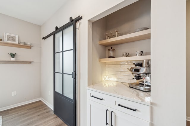 bar featuring white cabinets, a barn door, light wood-type flooring, a healthy amount of sunlight, and light stone counters