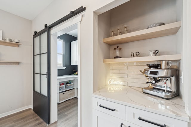 bar with white cabinetry, a barn door, light stone countertops, and light hardwood / wood-style flooring