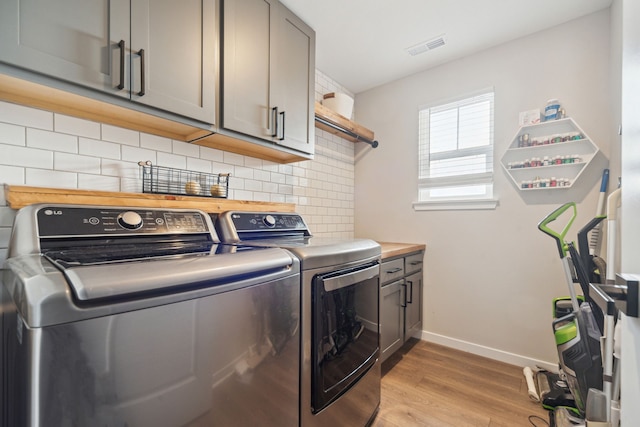 laundry room featuring cabinets, washing machine and dryer, and light hardwood / wood-style flooring