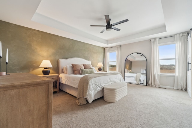 carpeted bedroom with ceiling fan and a tray ceiling