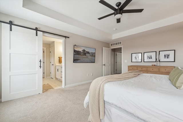 bedroom with ceiling fan, a barn door, ensuite bathroom, light colored carpet, and a tray ceiling