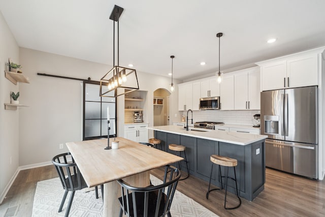 kitchen featuring stainless steel appliances, a barn door, white cabinetry, hanging light fixtures, and an island with sink