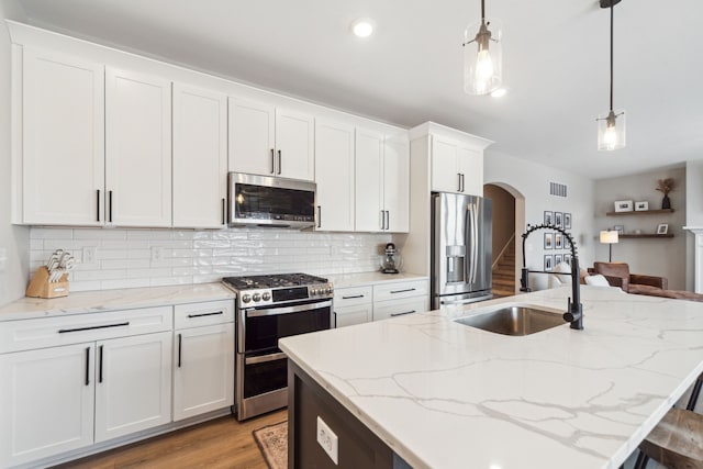 kitchen featuring hanging light fixtures, decorative backsplash, a center island with sink, white cabinets, and appliances with stainless steel finishes