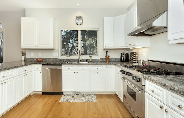 kitchen with wall chimney range hood, sink, dark stone countertops, appliances with stainless steel finishes, and white cabinetry