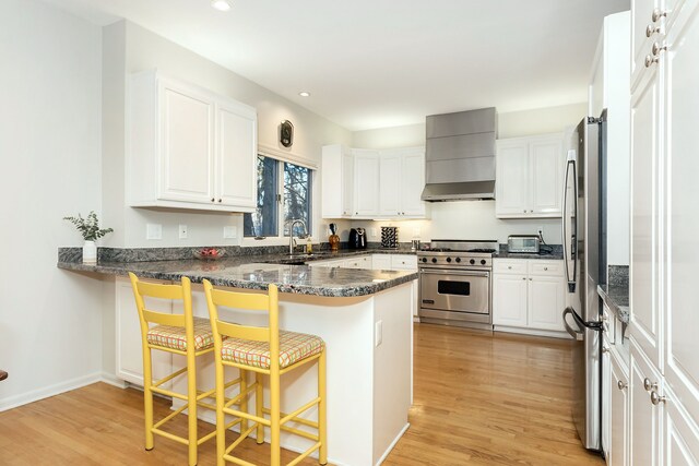 kitchen with kitchen peninsula, stainless steel appliances, white cabinets, and wall chimney exhaust hood