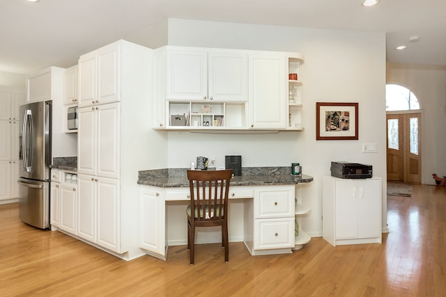 kitchen with stainless steel fridge, white cabinetry, built in desk, dark stone counters, and light wood-type flooring