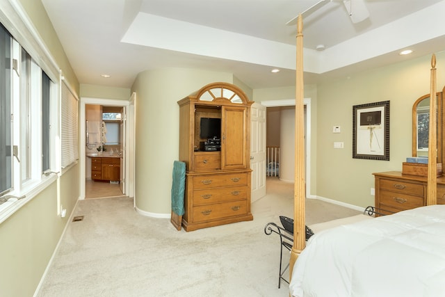 bedroom featuring light carpet, connected bathroom, a skylight, and a raised ceiling