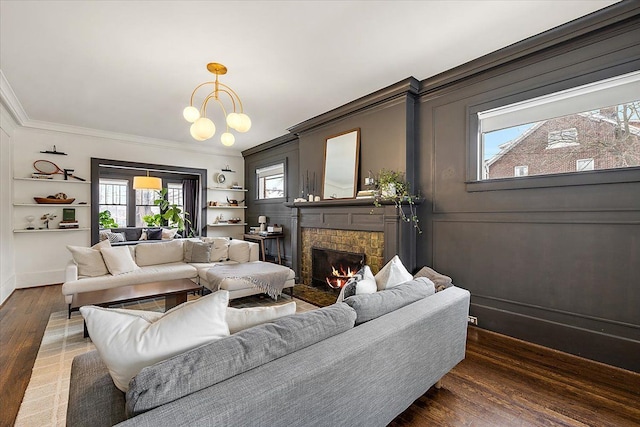 living room featuring dark wood-type flooring, ornamental molding, a chandelier, and a stone fireplace