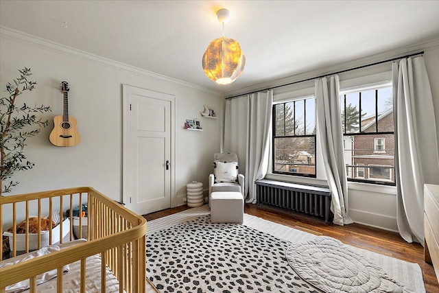 bedroom featuring hardwood / wood-style floors, a nursery area, radiator heating unit, and ornamental molding