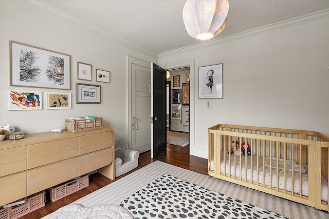 bedroom featuring a nursery area, ornamental molding, and dark hardwood / wood-style floors