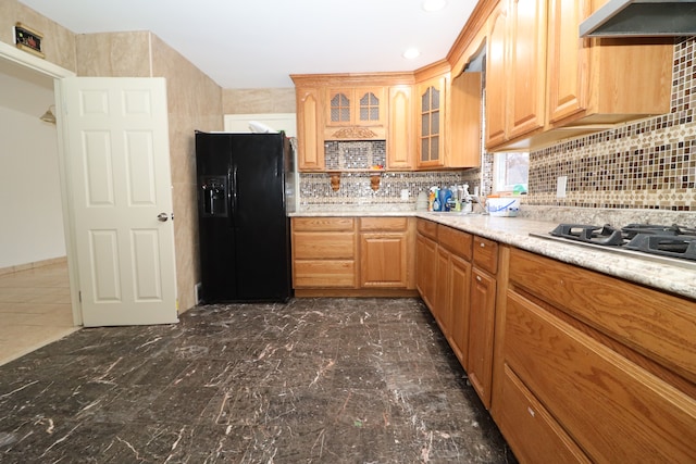 kitchen featuring backsplash, ventilation hood, black fridge, and stainless steel gas stovetop