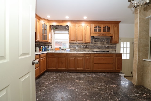 kitchen with backsplash, black stovetop, and range hood