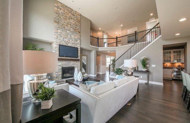 living room featuring dark hardwood / wood-style flooring, a stone fireplace, and a towering ceiling