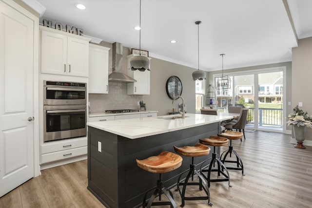 kitchen featuring a center island with sink, wall chimney exhaust hood, ornamental molding, and sink