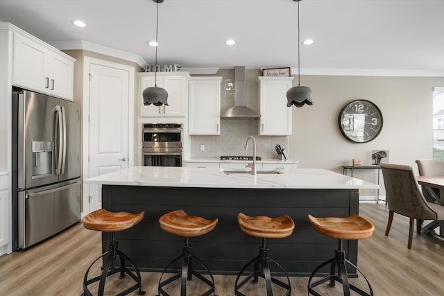 kitchen featuring white cabinets, appliances with stainless steel finishes, pendant lighting, and wall chimney range hood