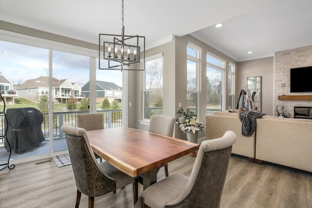 dining area featuring crown molding, a fireplace, light hardwood / wood-style floors, and an inviting chandelier