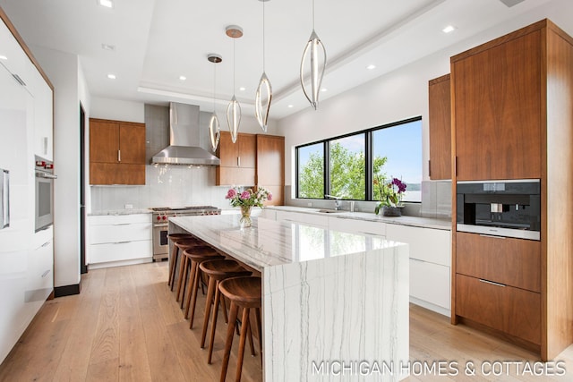 kitchen with appliances with stainless steel finishes, wall chimney exhaust hood, white cabinetry, a kitchen island, and hanging light fixtures