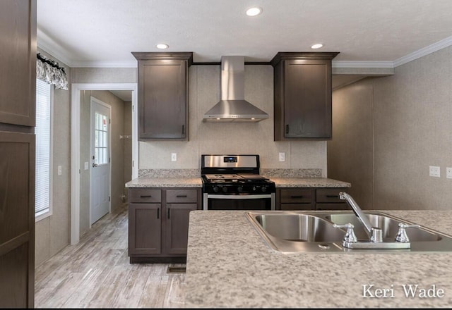 kitchen featuring sink, stainless steel range with gas stovetop, dark brown cabinetry, and wall chimney range hood