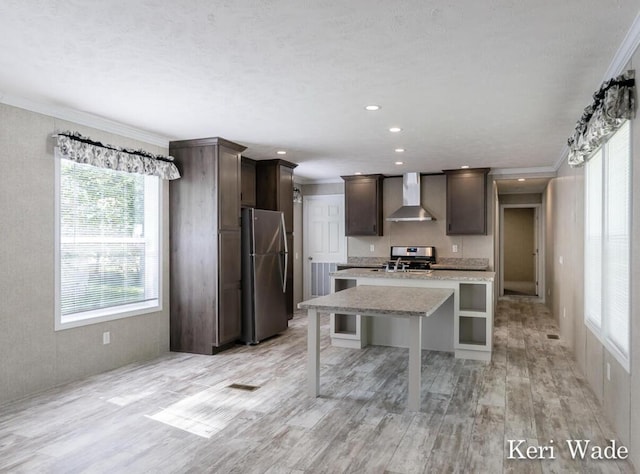 kitchen with appliances with stainless steel finishes, a kitchen breakfast bar, dark brown cabinets, wall chimney range hood, and an island with sink