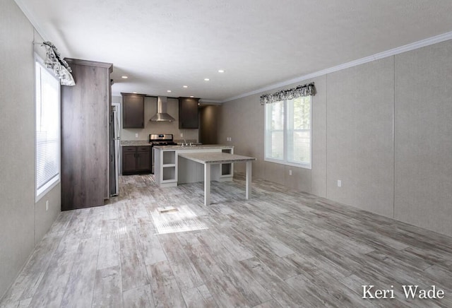 kitchen featuring a center island, wall chimney range hood, ornamental molding, dark brown cabinetry, and a breakfast bar area