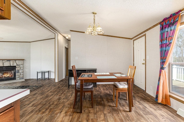 dining room with a chandelier, a textured ceiling, a stone fireplace, and dark wood-type flooring
