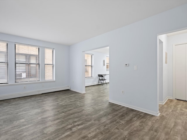 unfurnished room with wood-type flooring, a wealth of natural light, and a baseboard radiator